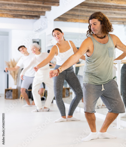 Diligent middle-aged man doing choreography at ballet barre in training hall during gym classes