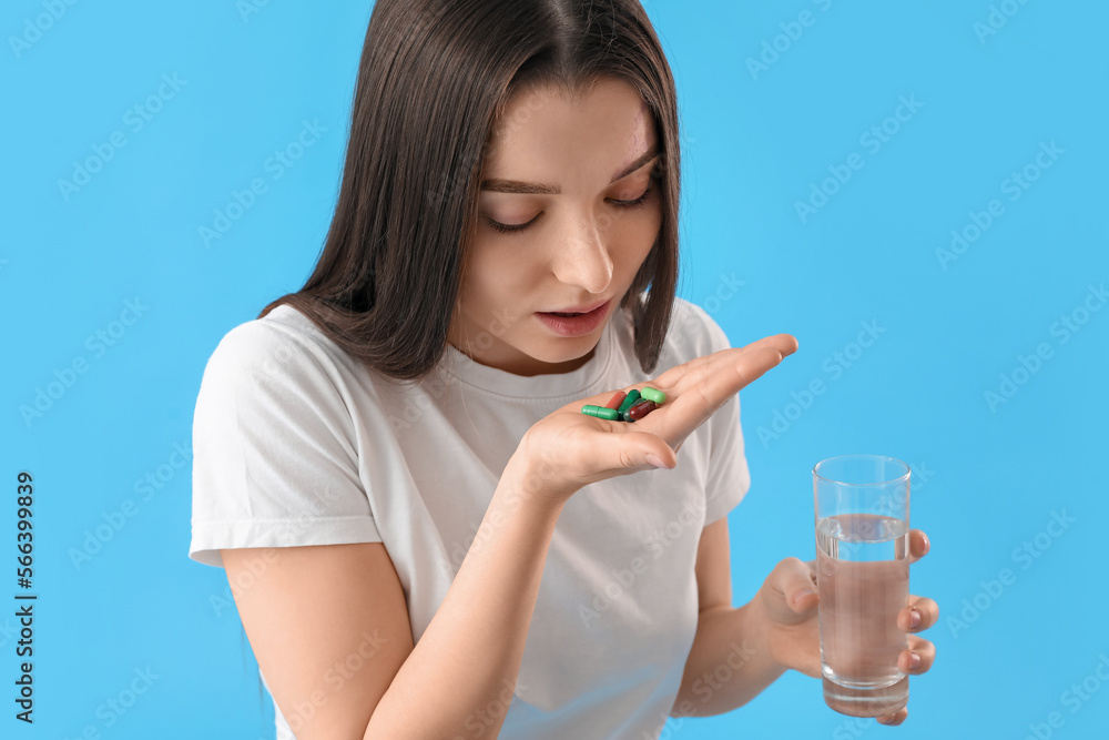 Young woman with glass of water taking vitamin supplement on blue background, closeup Young woman with glass of water taking vitamin supplement on blue background, closeup