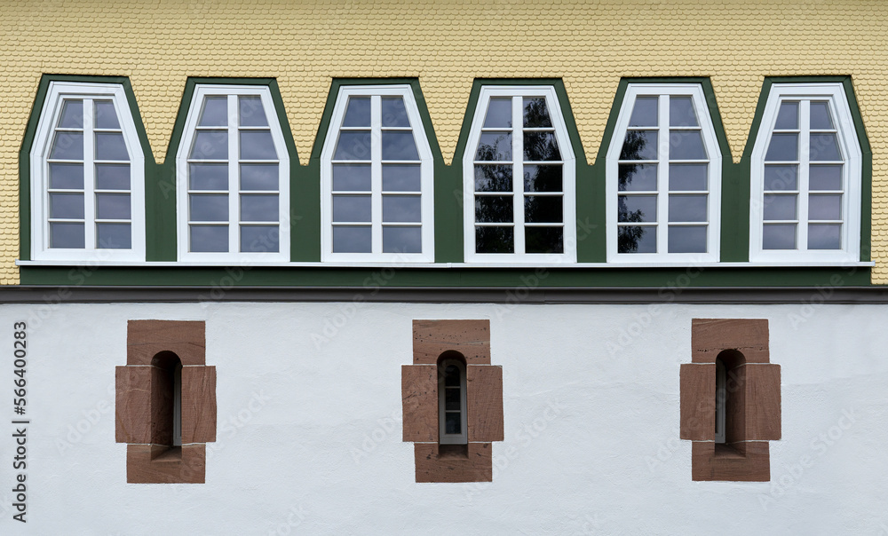 Reihe von trapezförmigen Fenstern über drei sehr schmalen Fenstern mit Steinrahmen in restaurierter Fassade