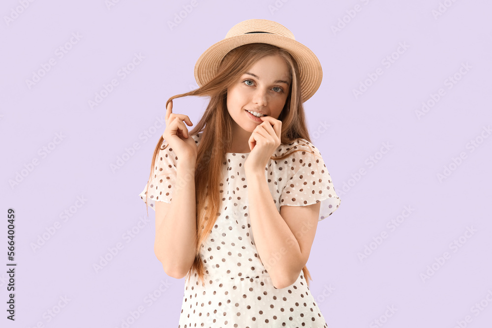 Young woman in hat biting nails on lilac background