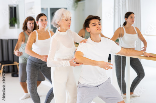 Senior woman choreographer and group of adult dancers practice ballet moves in classical dance school.