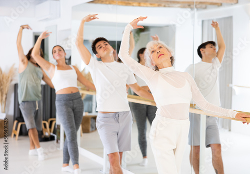 Slender elderly woman doing choreography at ballet barre during gym classes