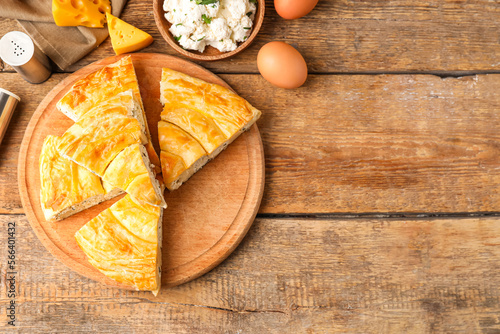 Board with pieces of delicious cheese pie and ingredients on wooden table