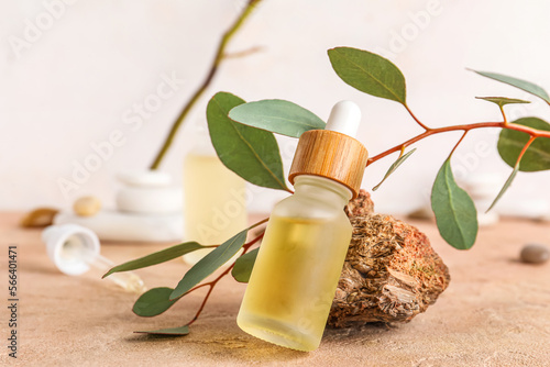 Composition with bottle of serum, stone and eucalyptus branch on color table, closeup