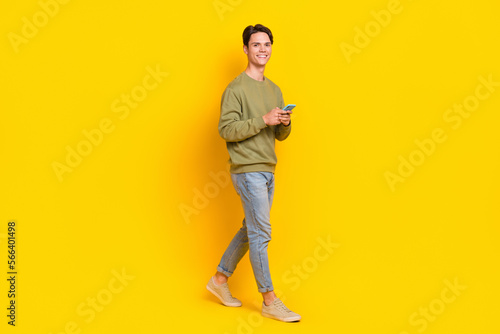 Full size profile photo of cheerful person hold smart phone walking isolated on yellow color background