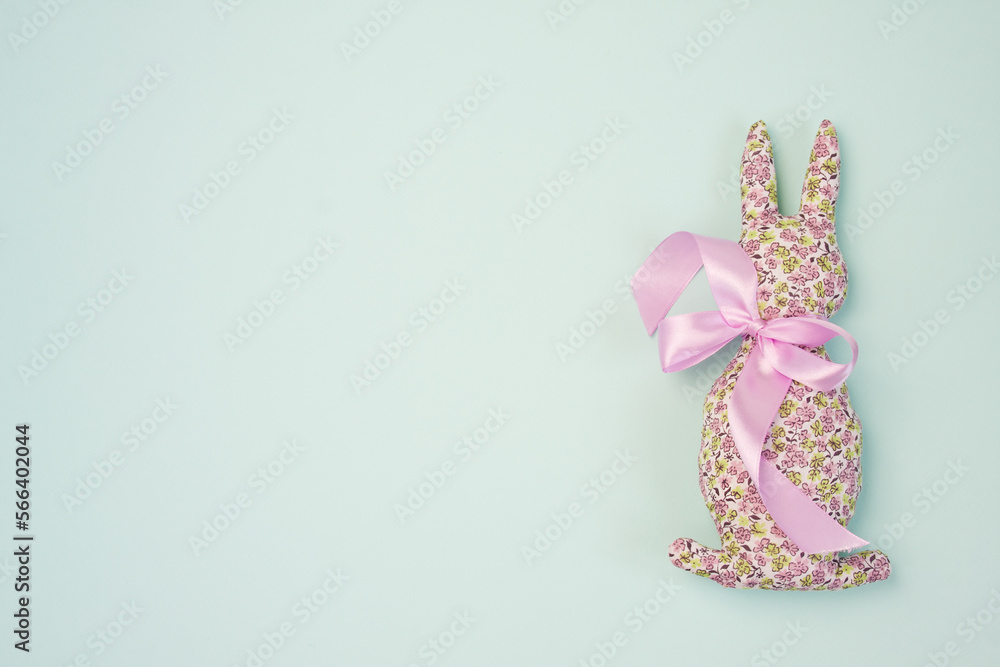 Decorative handmade Easter Bunny soft toy made of cotton fabric, decorated with pink satin ribbon. Isolated on blue background. Mockup for greeting card. Space for text. top view