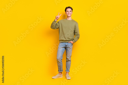 Full length photo of positive nice man wear street smart casual style clothes hand v-sign empty space isolated on yellow color background