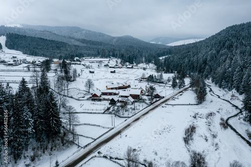 Aerial view of pine forest and a small village covered by snow in Carpathian Mountains of Romania, Rarau Mountains region. Cloudy weather conditions