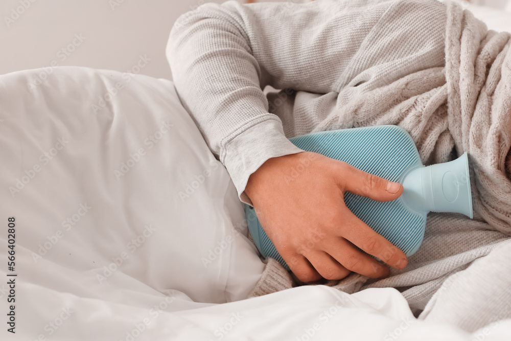 Ill man lying with hot water bottle in bedroom, closeup Ill man lying with hot water bottle in bedroom, closeup