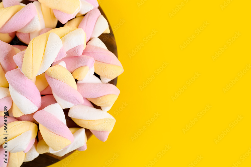 Board with tasty twisted marshmallows on yellow background