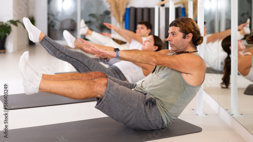 Diligent middle-aged man practicing pilates in training area during pilates classes