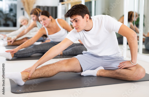 Slender young man engaging in pilates training in gym room during training session