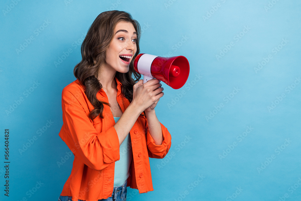 Photo portrait of young lovely lady holding megaphone announce huge sales dressed stylish orange outfit isolated on blue color background Photo portrait of young lovely lady holding megaphone announce huge sales dressed stylish orange outfit isolated on blue color background