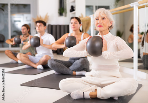 Elderly athletic woman performs exercises with ball in gym