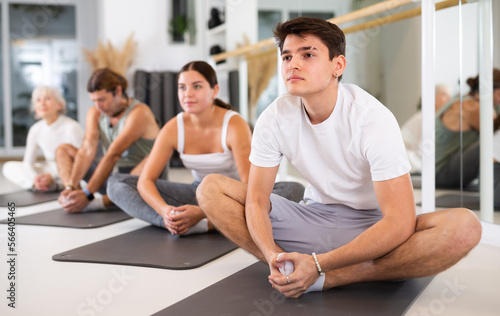 Sporty slender males and females doing exercises on a pilates mat during group training at gym. Healthy lifestyle concept.