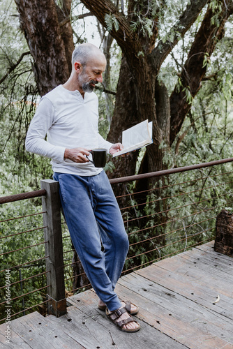 Hispanic man reading a book in the morning and holding coffee cup on the terrace of a country house in Mexico Latin America 