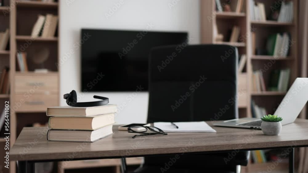 Shot of modern workplace, office with laptop, books, papers, eyeglasses, headset on wood table with large tv on white wall background. Shot of modern workplace, office with laptop, books, papers, eyeglasses, headset on wood table with large tv on white wall background.