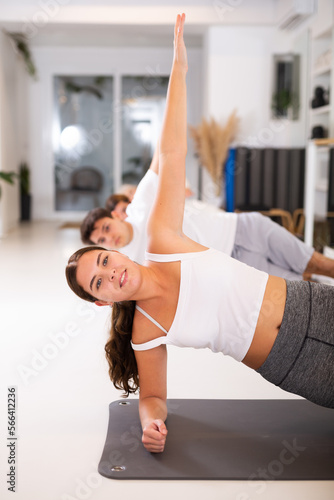 Gracile young woman doing pilates exercises on gray mat during workout session