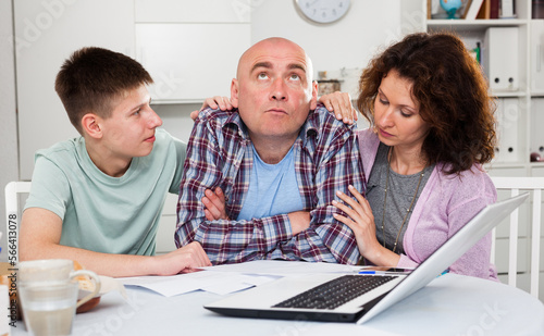 Loving wife with teenage son comforting upset man at home table..