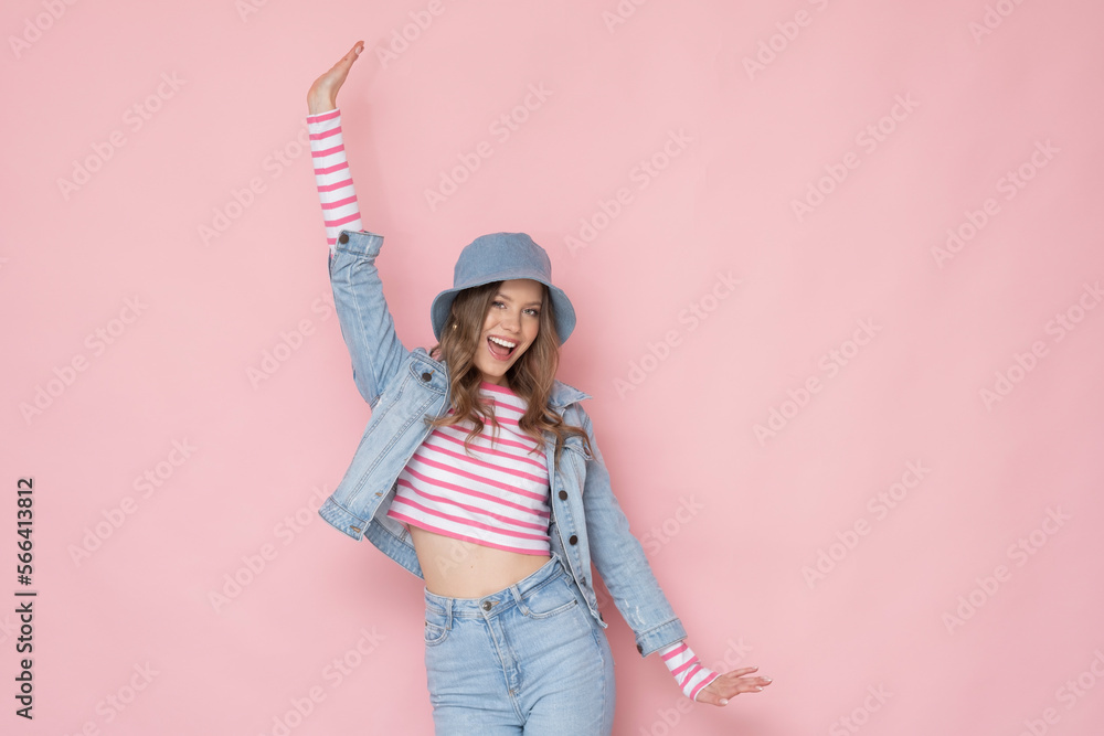 Very positive young woman in denim outfit on pastel pink background.