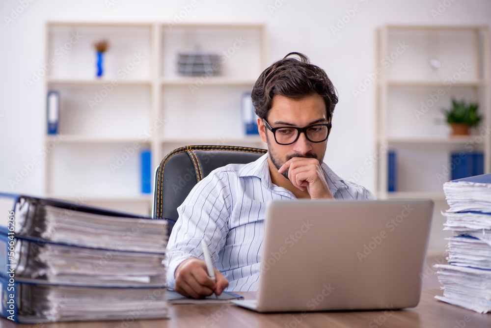 Young male employee unhappy with excessive work in the office Young male employee unhappy with excessive work in the office