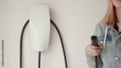 Kyiv, Ukraine. April, 2021. Woman takes switch-plug for an EV car fast charging. Electric car home charging installed at the residence's garage. High quality 4k footage
