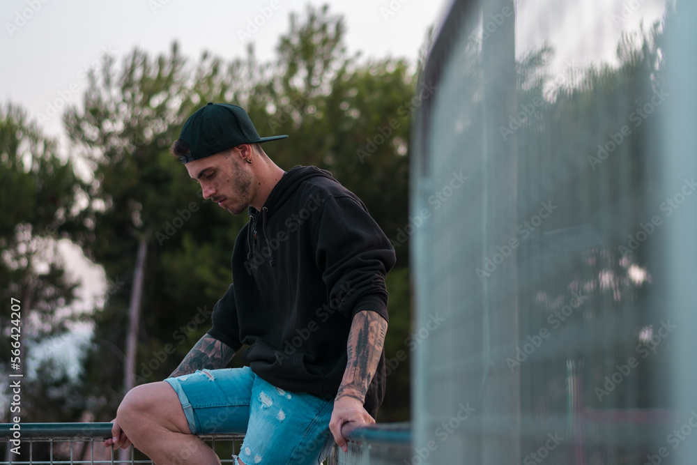 Man with tattoos in his arms is posing in a park Man with tattoos in his arms is posing in a park