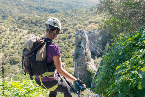 Adventure. Woman with helmet, harness and backpack. Descending in the mountains by a via ferrata. photo