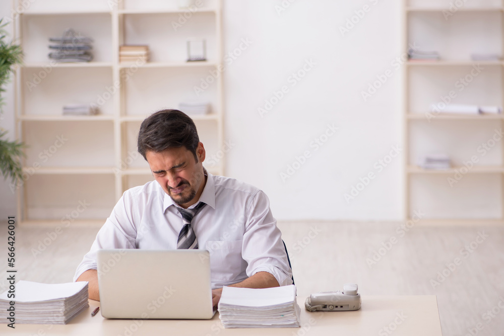 Young male employee unhappy with excessive work in the office Young male employee unhappy with excessive work in the office