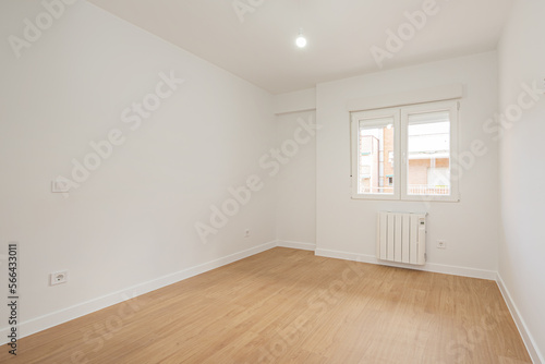 Empty living room with laminated flooring and recently finished smooth white walls with an aluminum radiator under a window of the same material