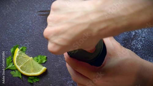 Hand opening a can of octopus on a dark blue table with lemon and parsley. Ready to eat.