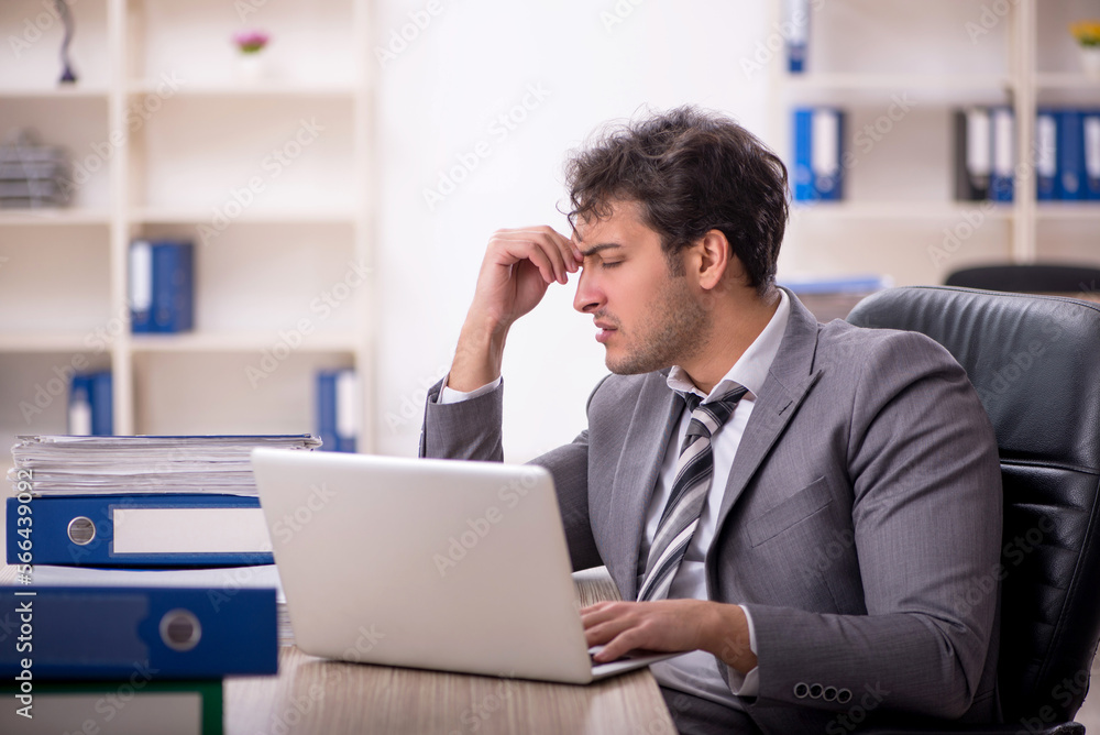 Young male employee unhappy with excessive work in the office Young male employee unhappy with excessive work in the office