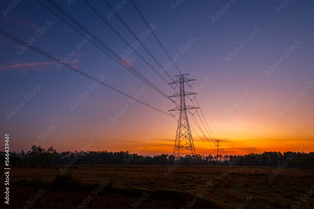 Silhouette electric pole and high voltage tower.High voltage transmission pole against morning sun in rice fields background.