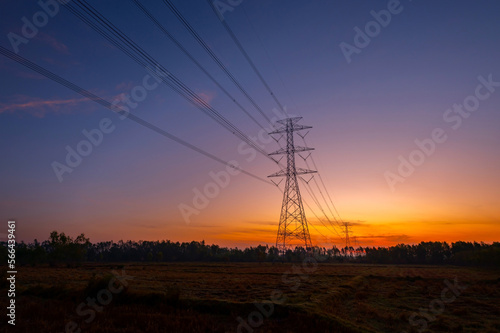 Silhouette electric pole and high voltage tower.High voltage transmission pole against morning sun in rice fields background.