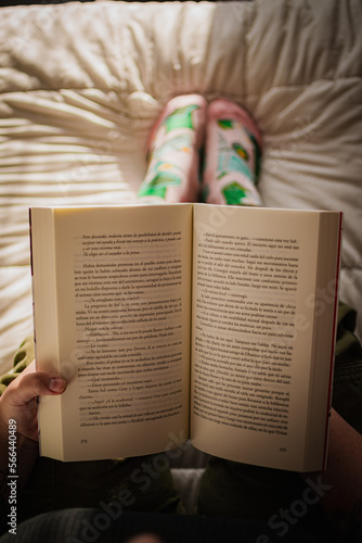 girl in white bed reading a book, green pants and pink socks