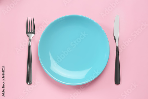 Clean plate and shiny silver cutlery on pink background, flat lay