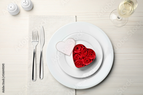 Beautiful table setting. Dishware and decorative heart shaped box with roses for romantic dinner on white wooden table, flat lay