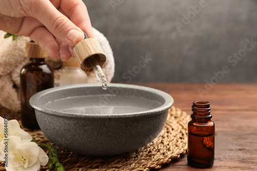 Woman dripping essential oil into bowl at wooden table, closeup. Aromatherapy treatment