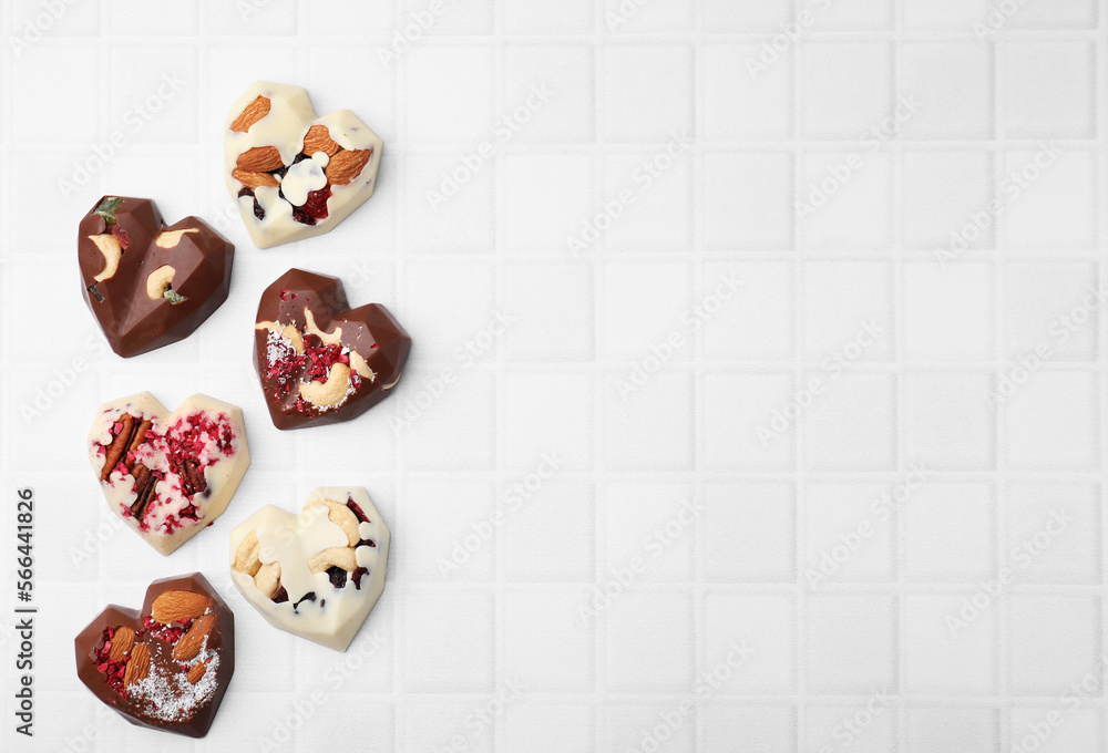 Tasty chocolate heart shaped candies with nuts on white tiled table, flat lay. Space for text Tasty chocolate heart shaped candies with nuts on white tiled table, flat lay. Space for text