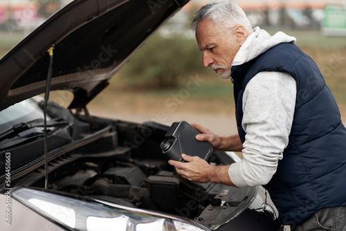 Experienced senior male driver adding environmental friendly oil in a car engine before the ride