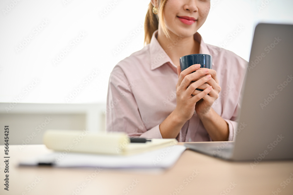 cropped image, Asian businesswoman holding a cup of coffee while working at her office desk. cropped image, Asian businesswoman holding a cup of coffee while working at her office desk.