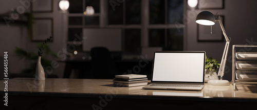 Modern office workspace at night with low light from table lamp, laptop screen mockup