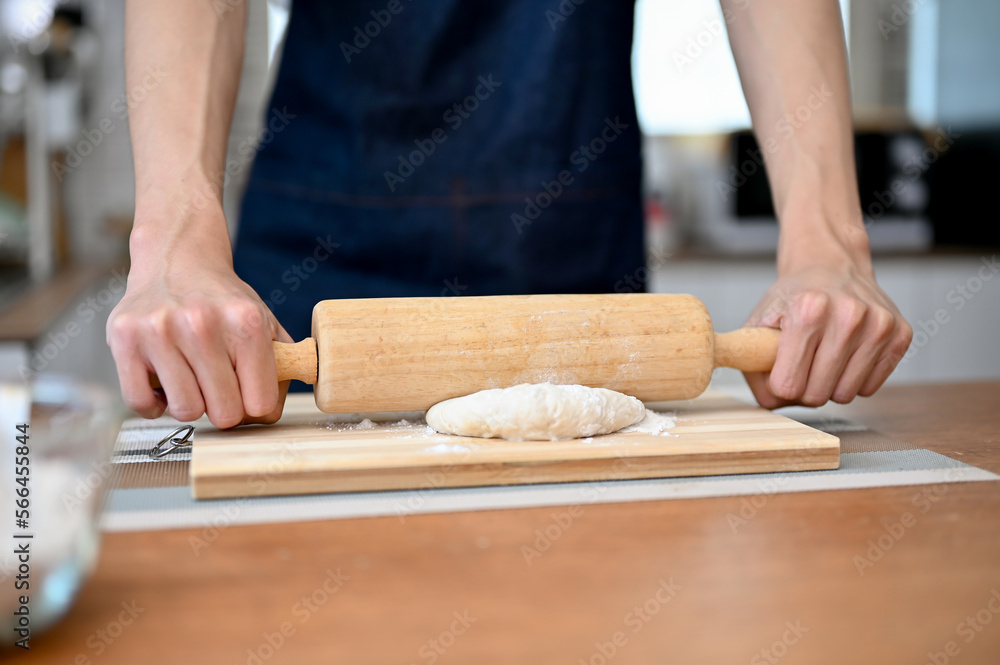 Close-up hands image of a man wearing apron holding a rolling pin, making dough on kitchen table Close-up hands image of a man wearing apron holding a rolling pin, making dough on kitchen table