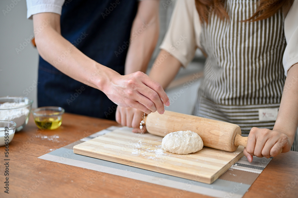 Lovely couple making dough together in the kitchen, kneading raw dough with a rolling pin.