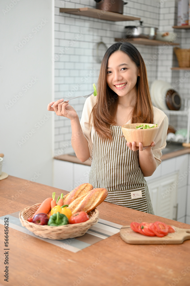 Portrait of an attractive and smiling young Asian woman wearing apron, holding a salad bowl