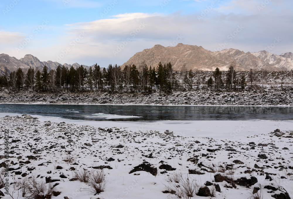 Snow-covered rocky banks of a melted river flowing down from the mountains through a valley in the mountains.