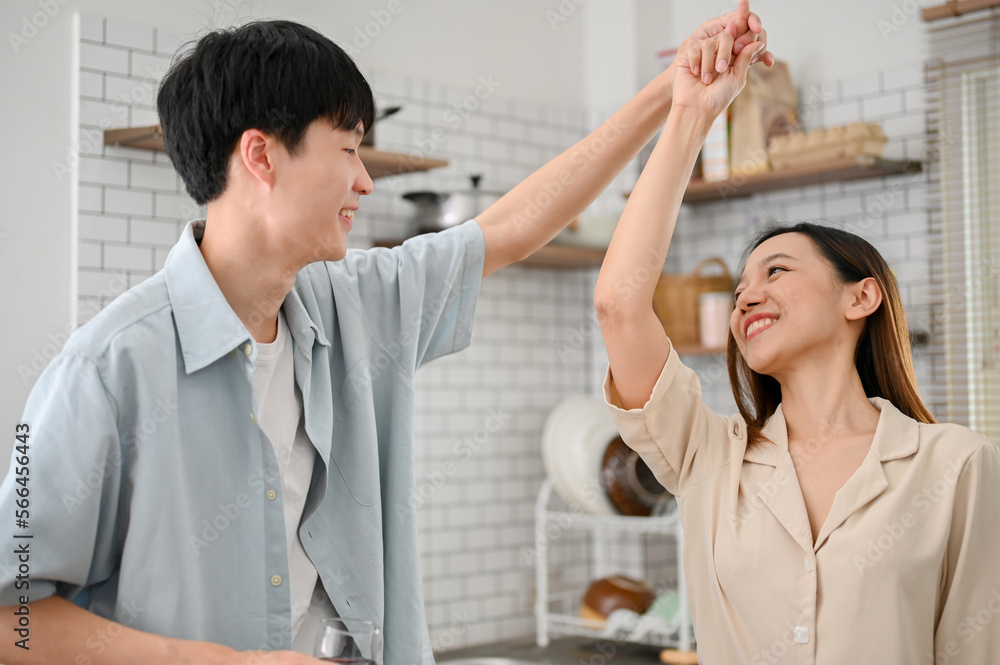 Obraz premium Loving and playful Asian couple dancing in the kitchen while preparing breakfast.