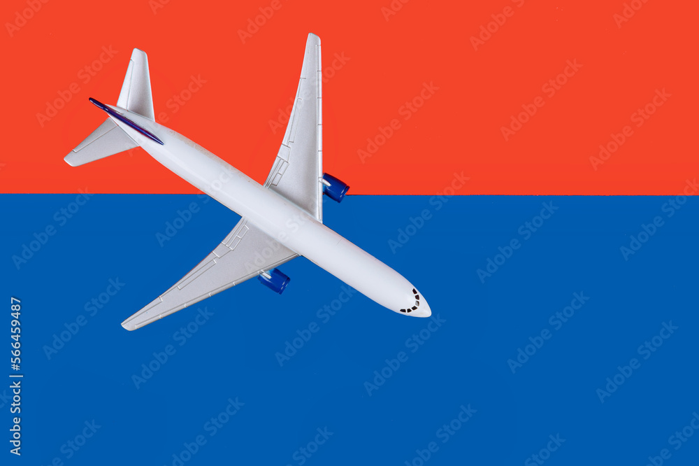 Against background of bright red and blue there is white model airplane passenger