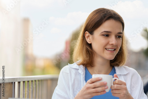Young confident smiling woman holding cup of coffee looking away sitting in cafe. Morning, coffee break concept