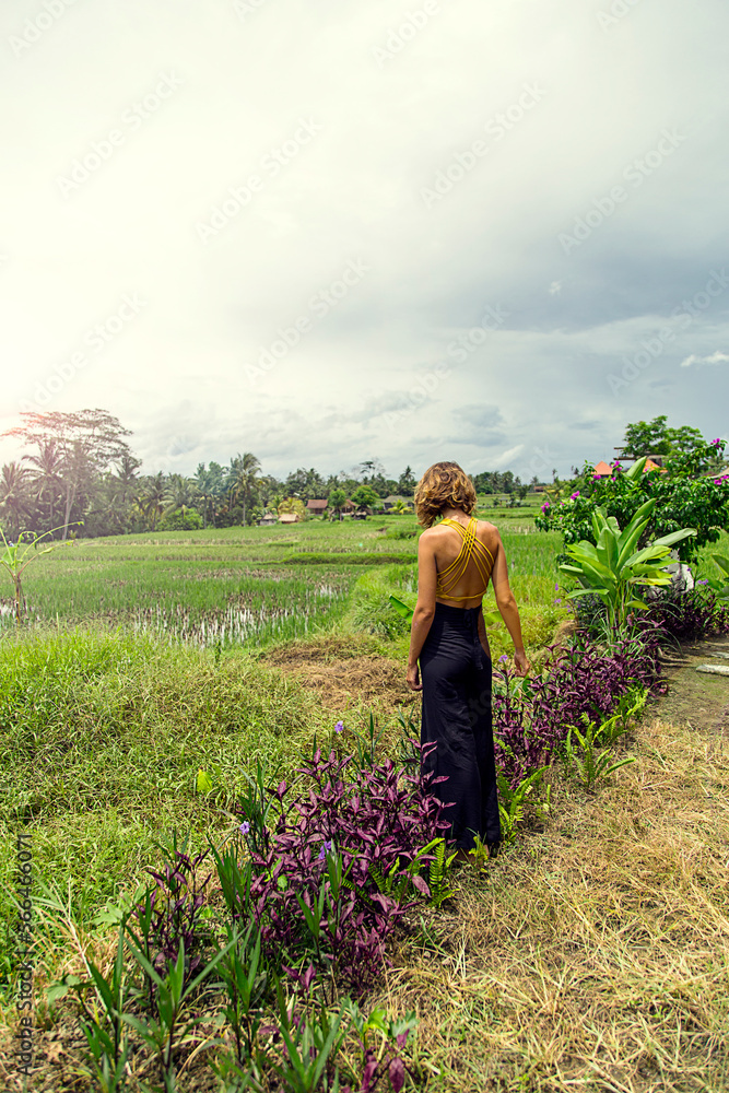 Fototapeta premium Caucasian woman, blonde, in yellow and black dress standing among the flowers and rice fields.